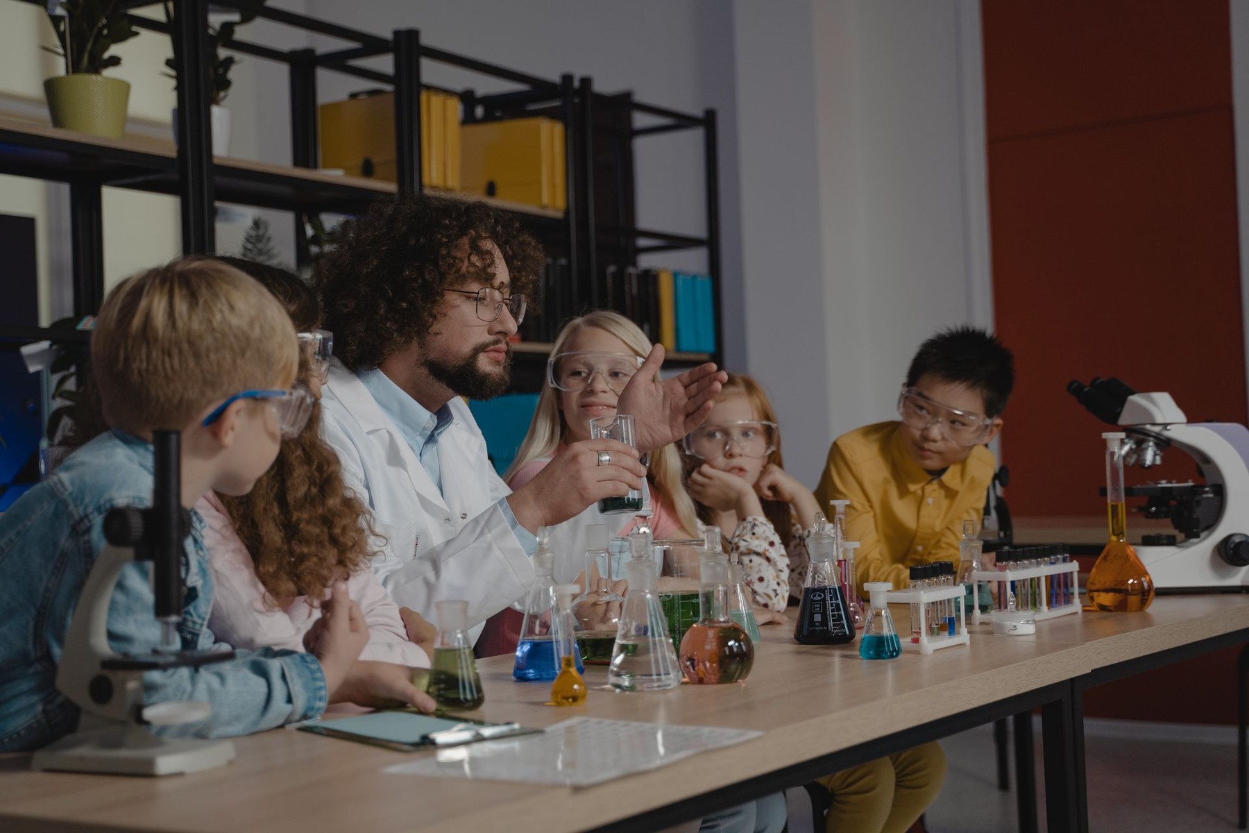 Adult mentor leading a science activity with children around a table of experiments