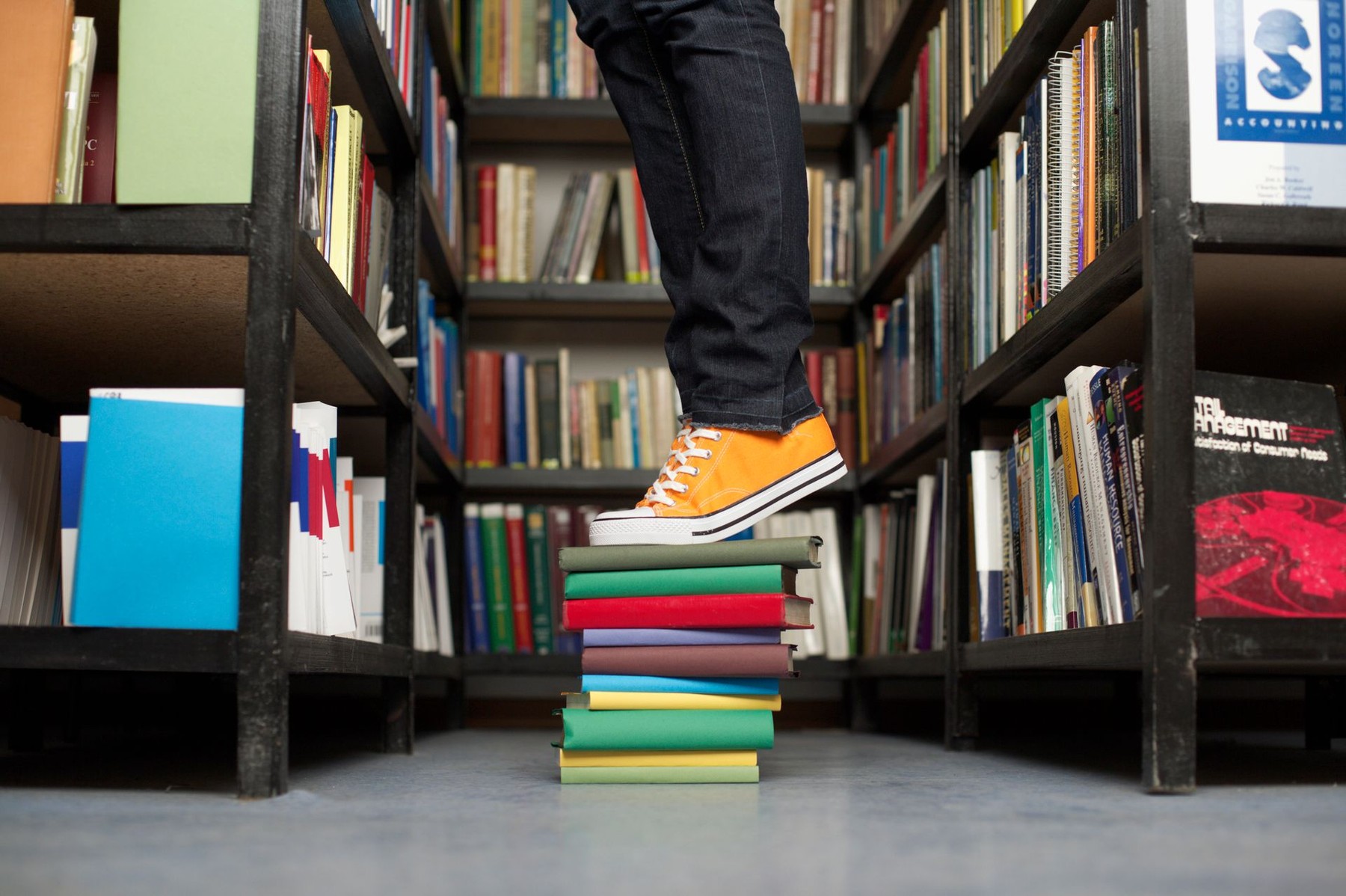 Bookshelves in a library with a person standing on stacked books to reach more resources